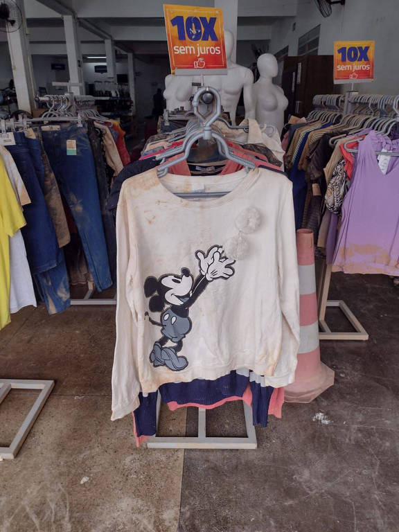 A foto mostra roupas manchadas de lama penduradas em cabides na loja do Grupo Zema em Brumadinho (MG)