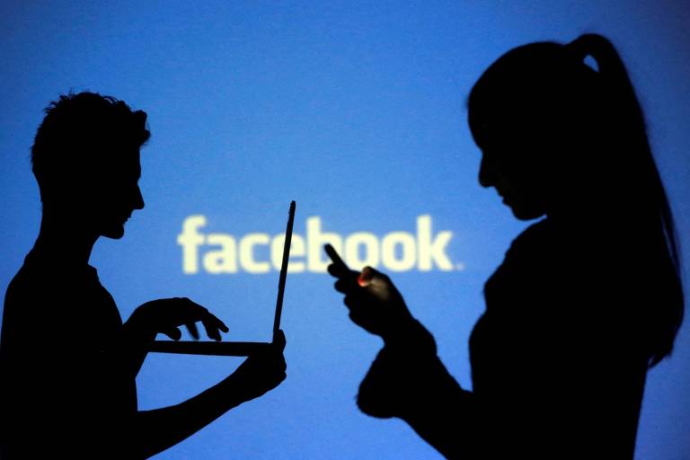 Pessoas posam em frente a logotipo do Facebook enquanto usam redes sociais em laptop e celular 