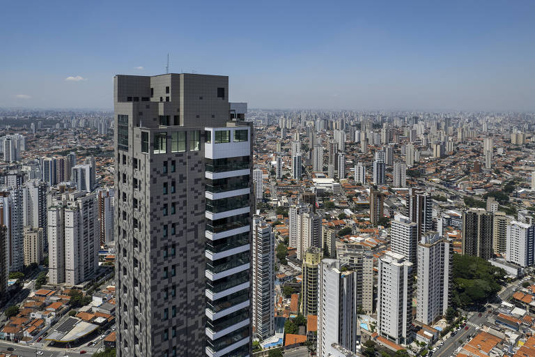 Imagem mostra vários prédios da cidade de São Paulo. Em primeiro plano, há um prédio residencial de luxo cinza.