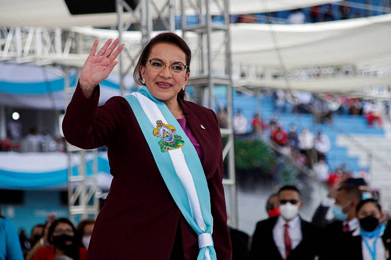 A nova presidente de Honduras, Xiomara Castro, acena com a mão direita em Tegucigalpa, a capital do país; ela usa óculos e está com a faixa presidencial, nas cores azul claro e branco, sobre uma roupa cor de vinho