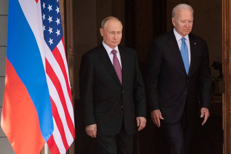 Ao lado das bandeiras da Rússia e do EUA, Biden e Putin, dois homens brancos e de terno, em pé, lado a lado