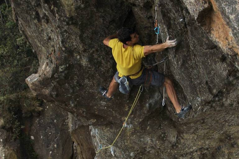 Um homem, usando uma corda de segurança, está escalando um paredão de pedra