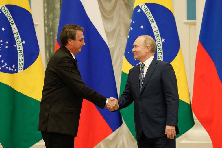 Biden e Bolsonaro se cumprimentam com as mãos, ao fundo bandeiras dos dois países