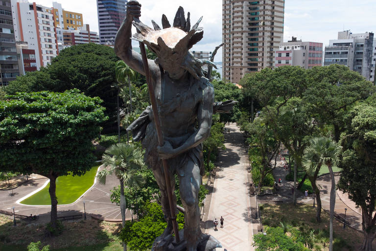 parque com enorme estátua de bronze de homem indígena segurando uma lança