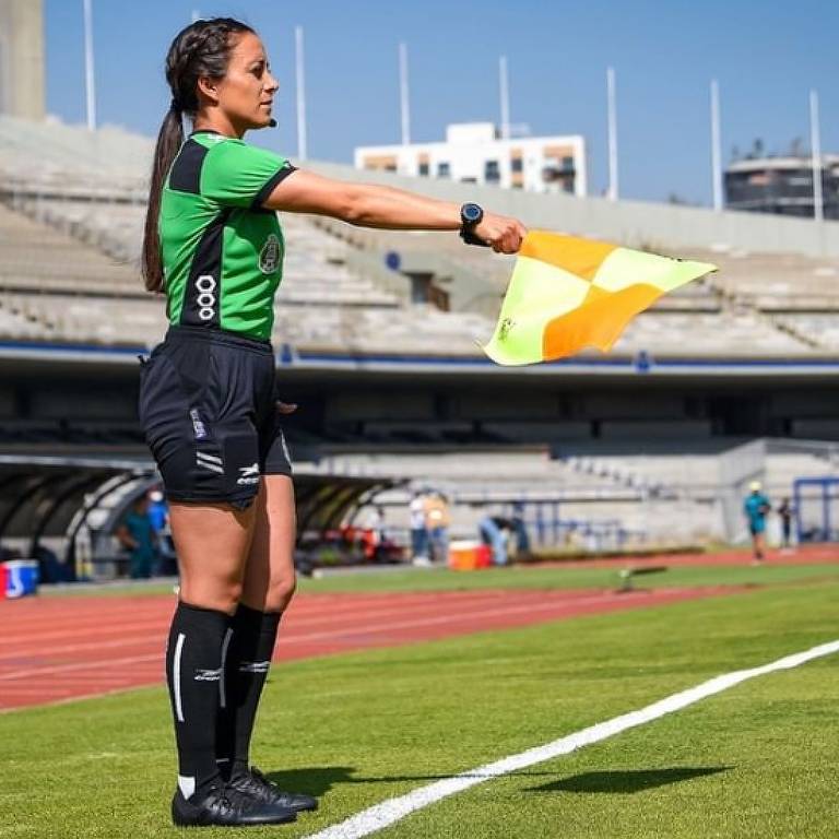 Valeria Andrade estica a bandeira das cores amarelo e laranja com o braço direito ao atuar como assistente de arbitragem em Pumas x América, no Campeonato Mexicano feminino