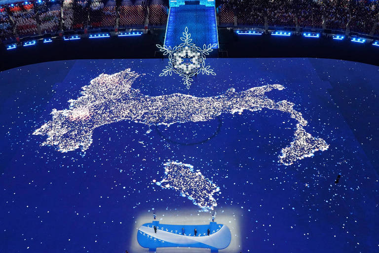 mapa da Itália, que parece uma bota, está projetado em chão de estádio. no alto, o símbolo de um floco de neve, que representa os jogos de inverno 