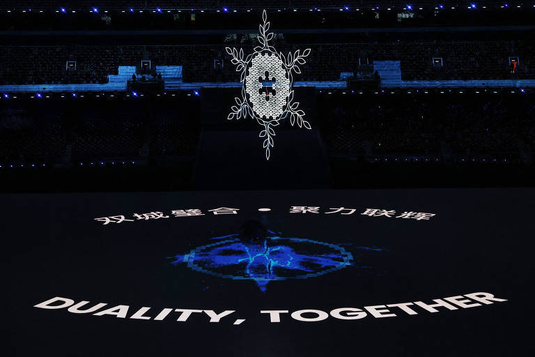 o floco de neve, símbolo das olimpíadas de inverno, está içado em um estádio. no chão, estão projetadas em inglês e chinês as palavras "dualidade, juntos"