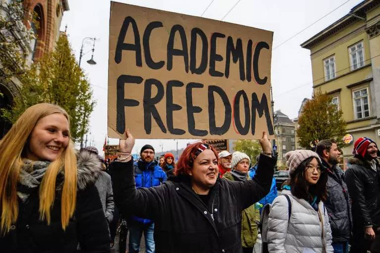 Mulheres vestidas com casacos levantam cartazes com inscrição "liberdade acadêmica" em protesto na rua 