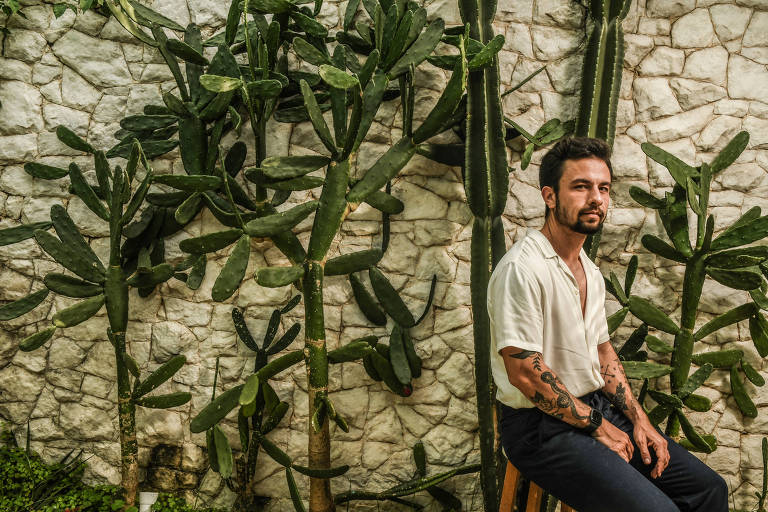 Luca Scarpelli, homem tatuado diante de muro branco com plantas do tipo cacto
