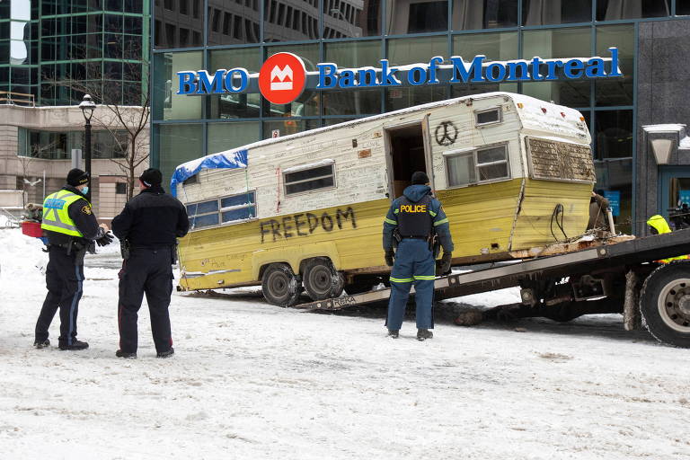 Veículo de manifestante antivacina é rebocado em rua com solo coberto de neve em Ottawa, no Canadá; do lado esquerdo, dois homens observam