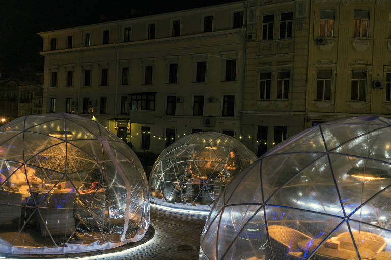 Pessoas jantam em globos transparentes instalados em um pátio 