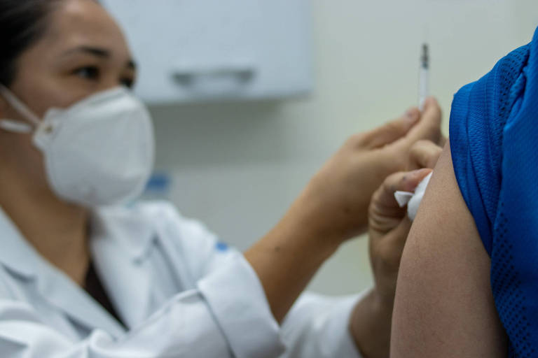 Auxiliar de enfermagem aplicar a vacina no braço direito de paciente em São Paulo