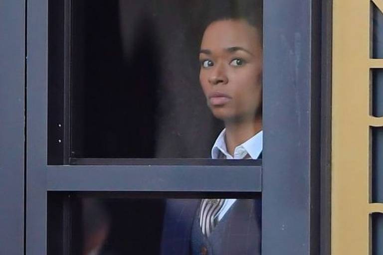 Cena de filme em que uma mulher negra olha através de uma janela de vidro