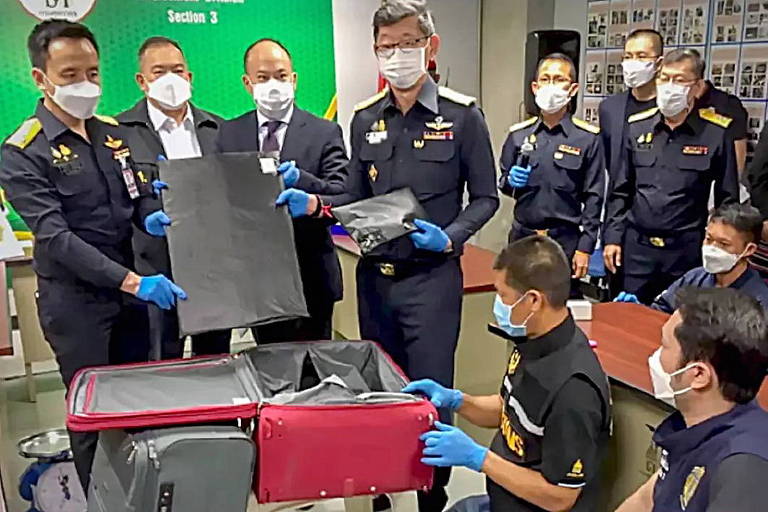 policiais com máscara mostra fundo de mala em sala de aeroporto