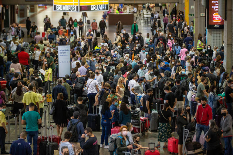 A imagem mostra uma multidão no saguão de um aeroporto