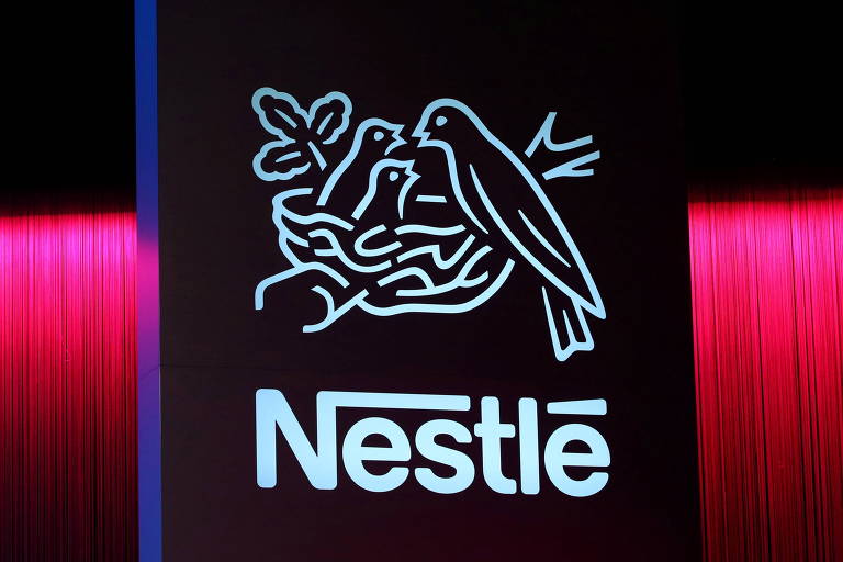 Logo da Nestlé, aparece em faixa, à frente de iluminação vermelha.