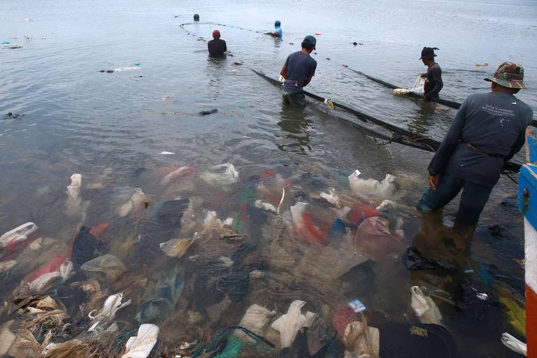 Rio cheio de lixo e pescadores estendendo rede em meio ao lixo