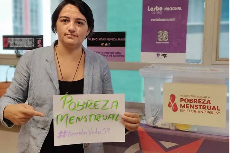 A socióloga Carla Ayres segura um cartaz com os dizeres "pobreza menstrual"