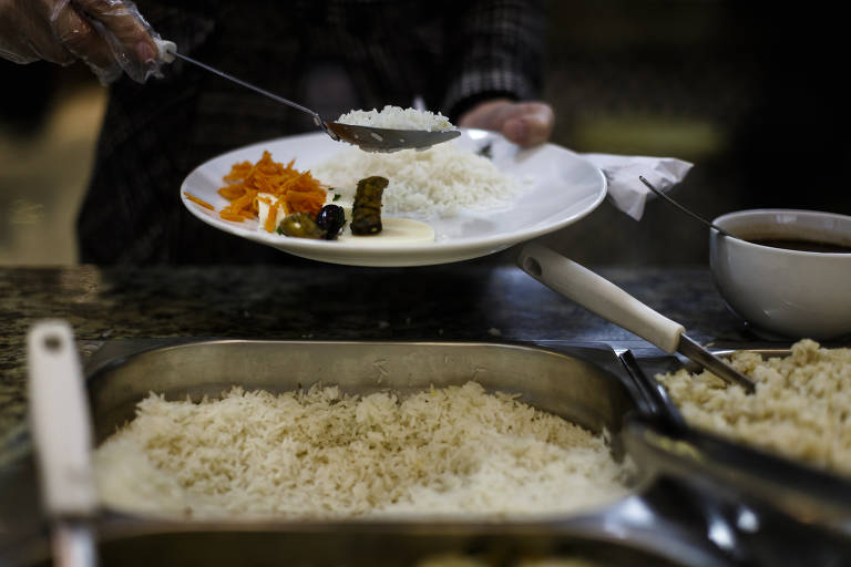 Homem leva colher de arroz branco ao prato, onde é possível ver outros alimentos