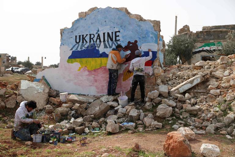 Imagem mostra um grupo de artistas escrevendo a palavra "Ucrânia" em inglês, em meio a destroços.