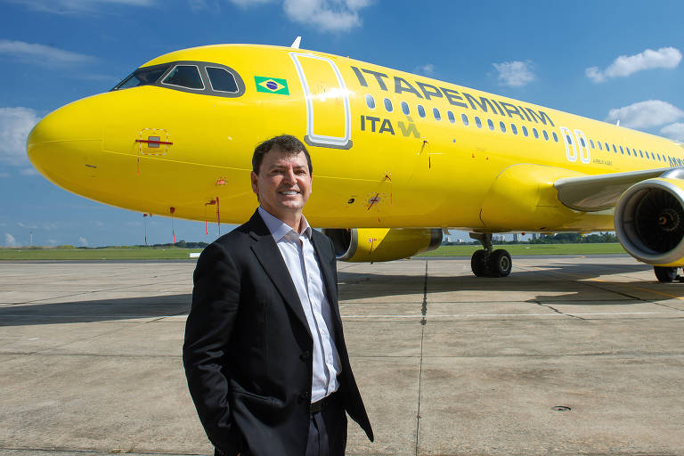 homem branco de terno preto em frente a um avião amarelo