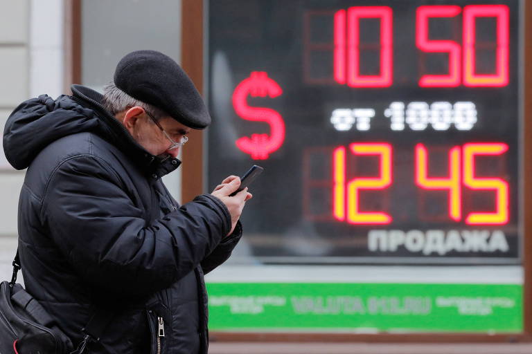 Homem usa seu celular em frente a um painel da cotação dólar-rublo