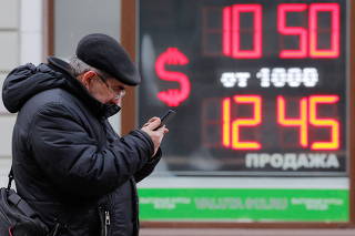 A man uses his smartphone near a board showing currency exchange rates of U.S. dollar against the Russian rouble in Saint Petersburg