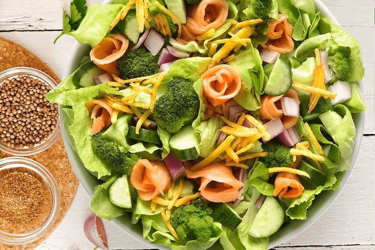 Foto tirada de cima do prato mostra uma salada de folhas verdes e rolinhos de salmão defumado