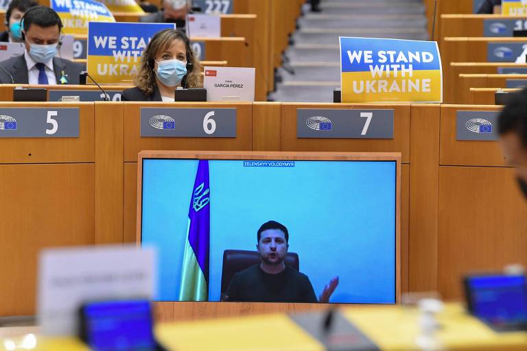 O presidente ucraniano discursa por vídeo ao Parlamento Europeu; 'Nós estamos com a Ucrânia', dizem os cartazes