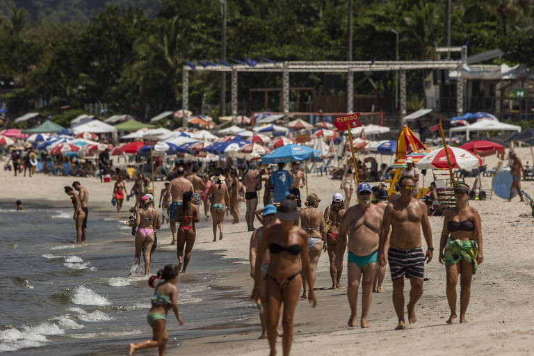 Pessoas caminhando na areia em praia do litoral norte de São Paulo.