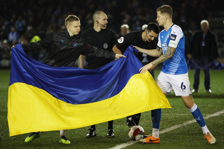 Oleksandr Zinchenko (esq.), do Manchester City, exibe bandeira da Ucrânia ao lado do capitão do Peterborough, Frankie Kent, em jogo da FA Cup