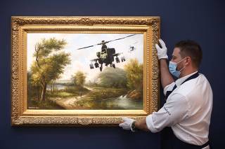 A Sotheby's employee poses with the artwork 'Vandalised Oils (Choppers)' by Banksy, ahead of auction at Sotheby's in London