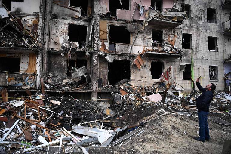 Homem tira foto de prédio destruído por bombardeio em Kiev, na Ucrânia