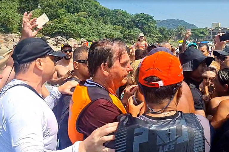 Presidente com colete salva-vidas é cercado por apoiadores em praia, com muito sol