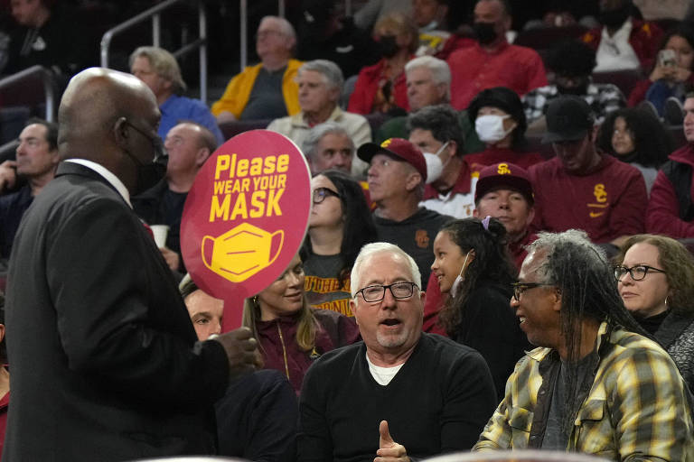 Funcionário do Galen Center, em Los Angeles, segura cartaz pedindo para a torcida usar a máscara de proteção em jogo do Southern California Trojans contra o Washington Huskies, pela NCAA