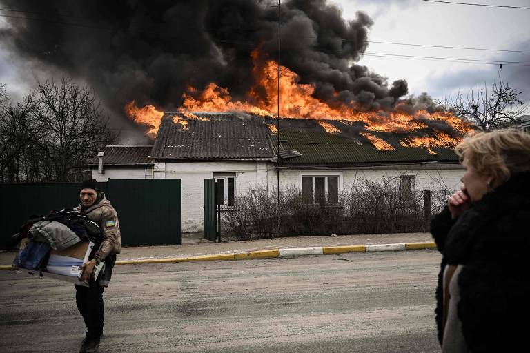 Ucraniano vestido com jaqueta militar retira pertences da casa em chamas em Irpin, perto de Kiev
