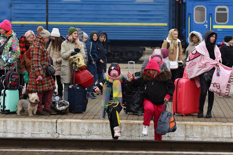 Refugiados ucranianos cruzam a linha do trem em Lviv para chegar à plataforma com uma composição para a Polônia