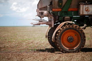 An agricultural worker drives a tractor spreading fertilizer in a soybean field, near Brasilia