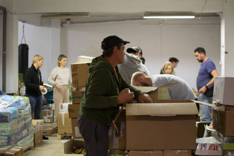 Em uma sala dechada, um grupo de pessoas jovens mexe em caixas com donativos para víitimas da guerra