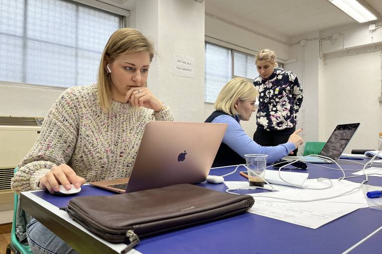 Mulher loira usa um computador enquanto está sentada em uma mesa