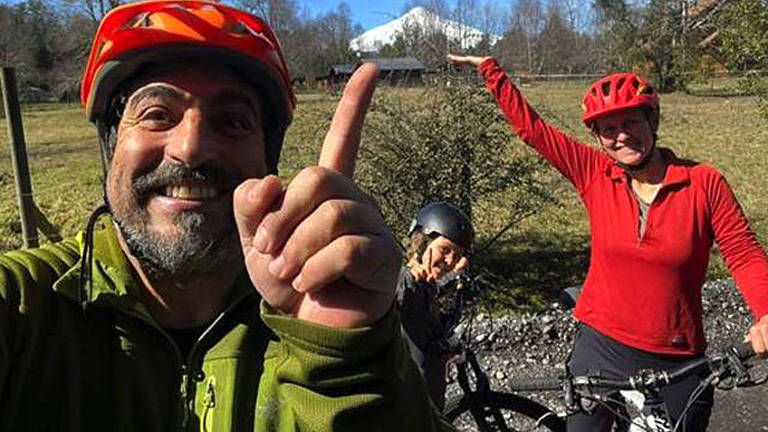 Homem, mulher e criança, em bicicletas, com capacete, sorrindo para selfie 