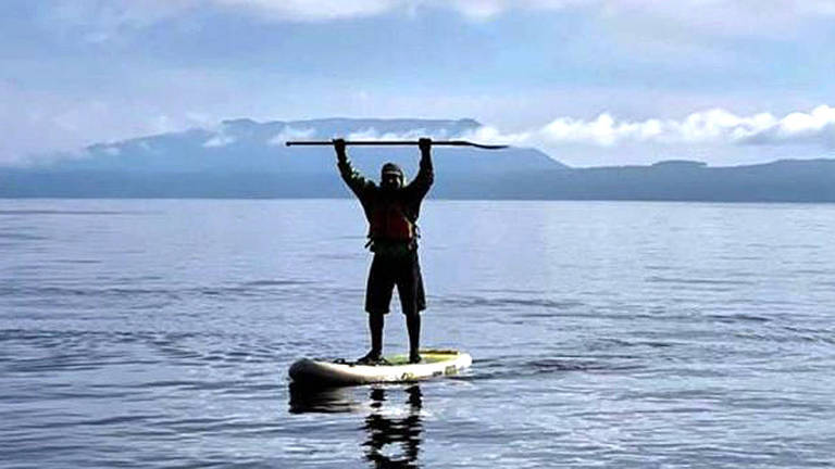 Homem com roupa de frio fazendo stand-up paddle em lago 