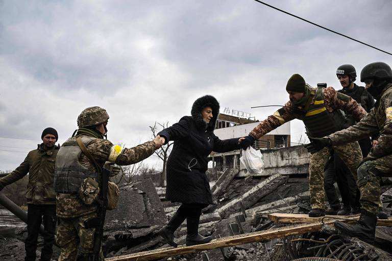 Mulher recebe ajuda de militares ucranianos para atravessar ponte destruída em Irpin, na Ucrânia