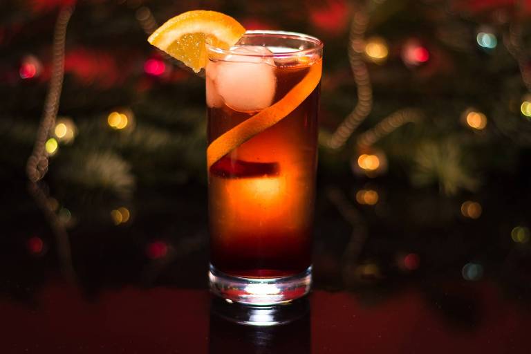 Coquetel em copo longo num bar escuro, com meia rodela de laranja na borda