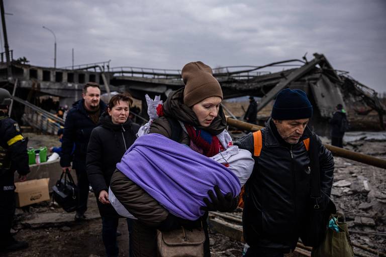 Mulher carregando bebê caminha sobre ponte parcialmente destruída na cidade de Irpin, na Ucrânia