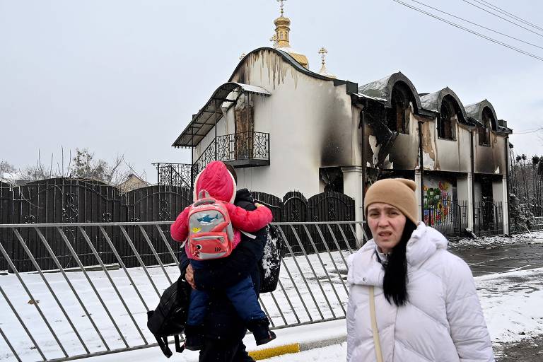 Mulher passa por prédio destruído ao deixar Irpin