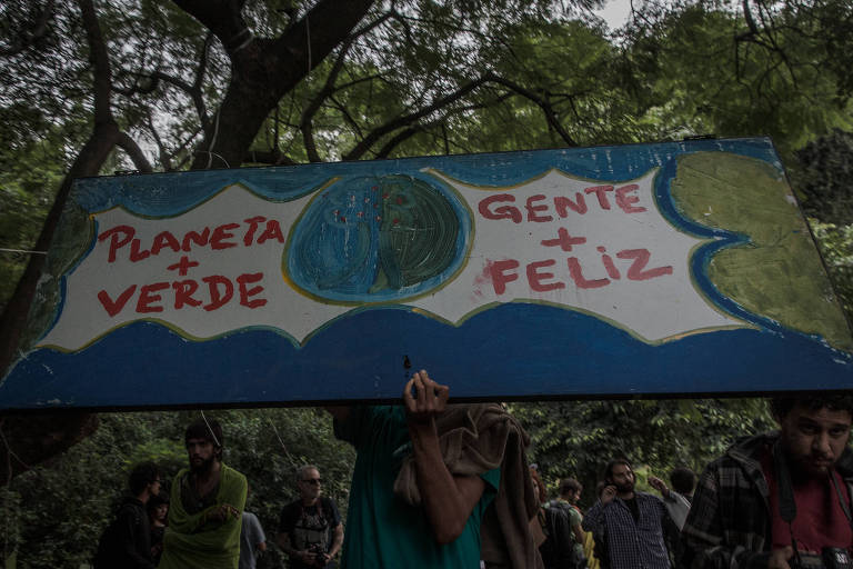Grupo de ativistas aparece em meio a árvores. Um deles segura uma placa em que é possível ler os dizeres "planeta + verde, gente + feliz".