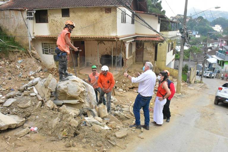Imagem mostra homens com capacetes em torno de escombros em Petrópolis