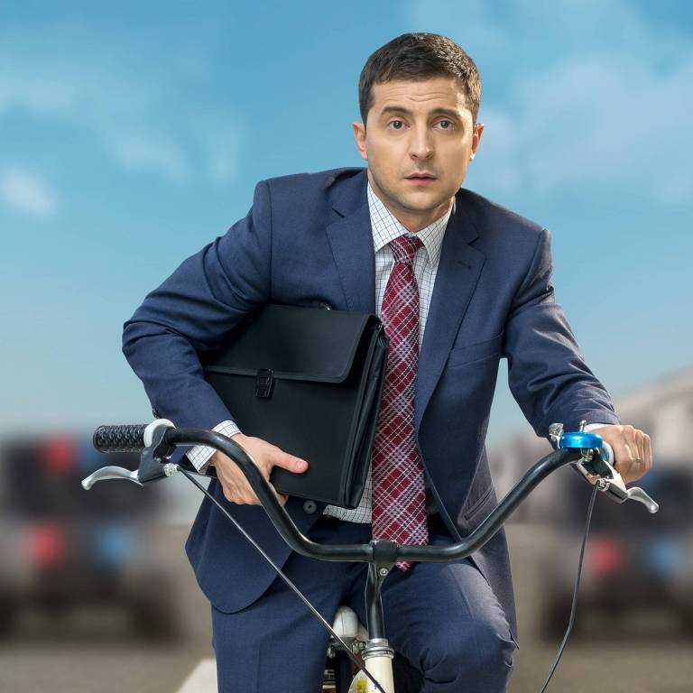 homem branco de terno guia bicicleta com uma expressão facial assustada