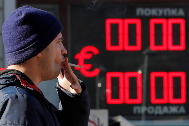 Homem passa fumando diante de painel eletrônico em casa de câmbio em São Petersburgo, na Rússia